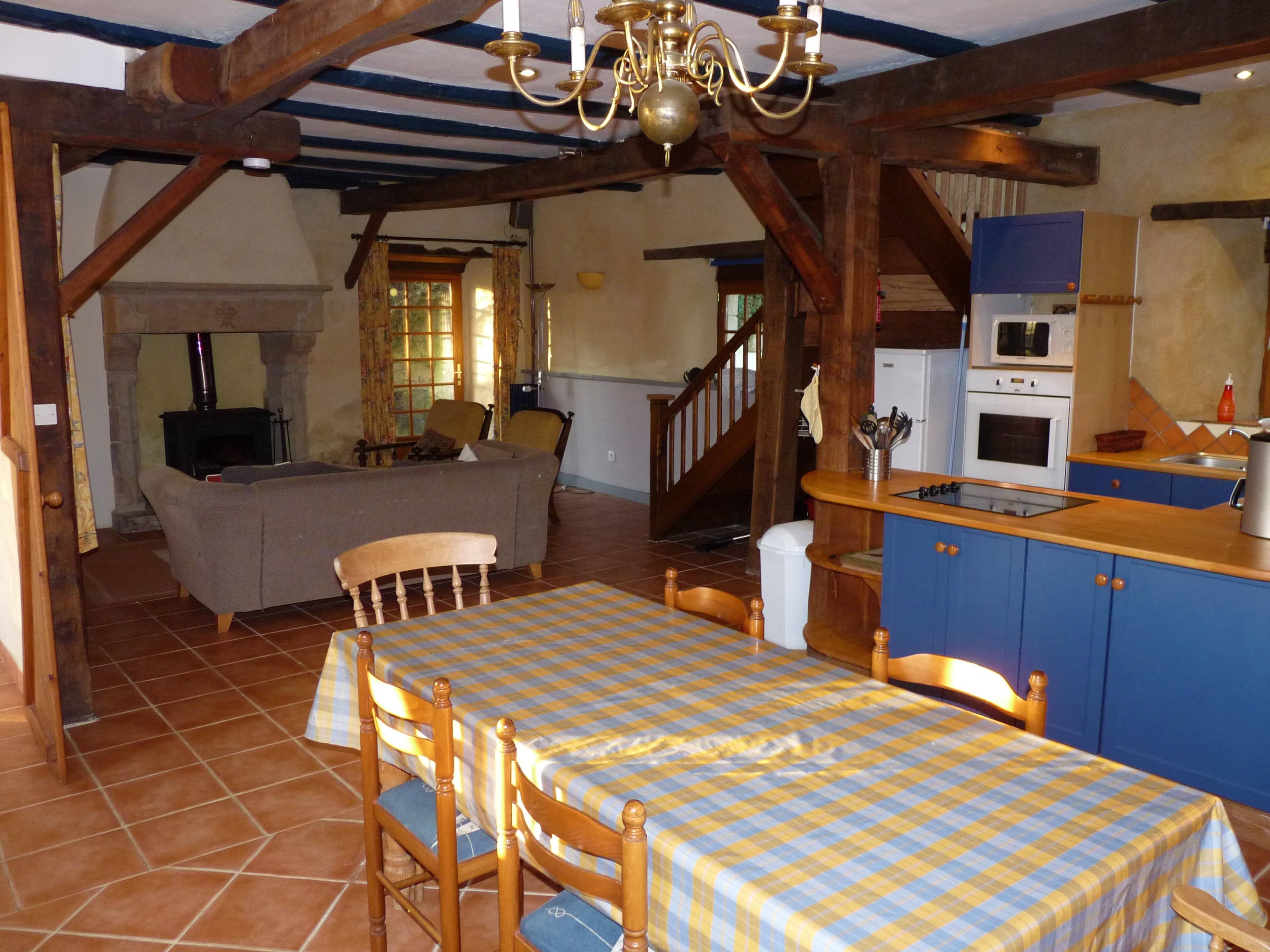 Bright and spacious dining room of La Julerie cottage in Brittany, France, featuring a large wooden table, comfortable chairs, and a fireplace. The room is beautifully decorated with rustic elements and offers stunning views of the surrounding countryside. Perfect for enjoying meals with family or friends during a holiday in Brittany.
